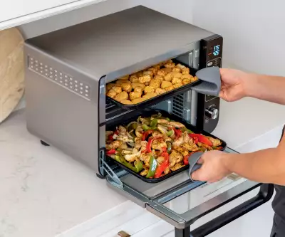 Someone pulling chicken nuggets and chicken and peppers out of the Ninja 12-in-1 Double Oven