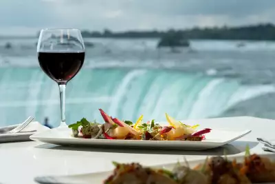 Niagara Parks | A glass of red wine and a dish sits in front of the view of the falls at Table Rock House Restaurant