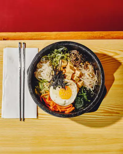 Korean Village Restaurant | Fried tofu bibimbap is served in a sizzling hot stone bowl with seasoned rice and veggies, and topped with an egg