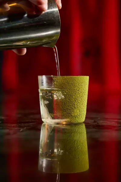 Vesper Bar Bangkok | A hand pours the Matcha Negroni cocktail