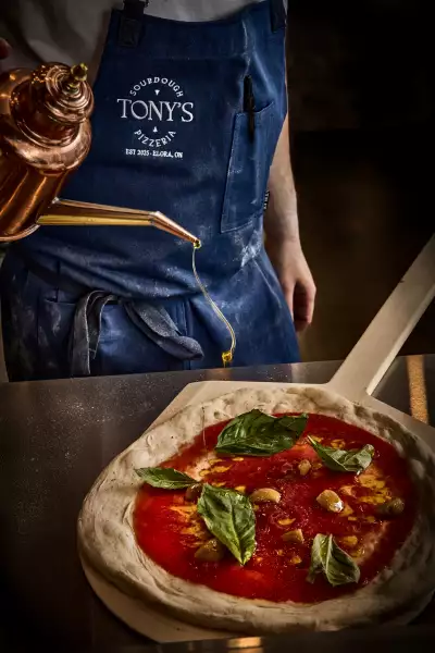 Tony's Sourdough Pizzeria in Elora | Chef Tony Bish pours olive oil onto the Basic Bish pizza