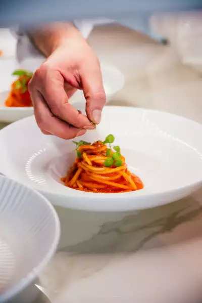 Don Alfonso's urban farm at Casa Loma | A hand adds a garnish to a plate of tomato pasta at Don Alfonso