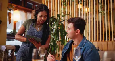 The Re-Seasoning Coalition | A customer listens to a waitress holding a tablet at a restaurant