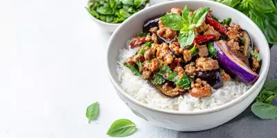 Thai Hom Mali rice | Thai basil eggplant with minced pork served over steamed jasmine rice, garnished with fresh basil leaves and dried red chilies in a white bowl