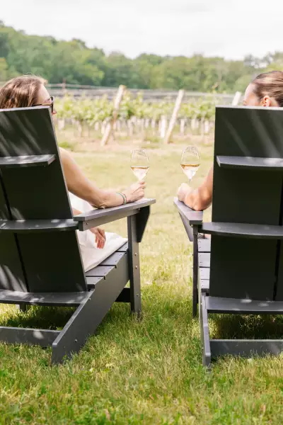 Mason Vineyard | Two guests enjoy a glass of wine in a Muskoka chair at Mason Vineyard Mason Vineyard | Two guests enjoy a glass of wine in a Muskoka chair at Mason Vineyard