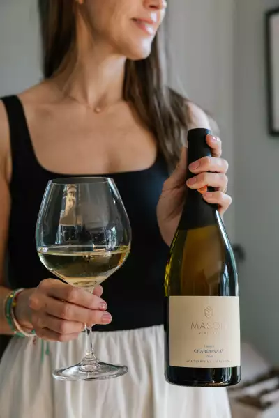 Mason Vineyard | A hand holds a glass and bottle of chardonnay at Mason Vineyard Mason Vineyard | A hand holds a glass and bottle of chardonnay at Mason Vineyard