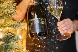 Trius Winery sparkling wine | A hand holds a bottle of Trius Brut and a glass of sparkling wine in front of a Christmas tree