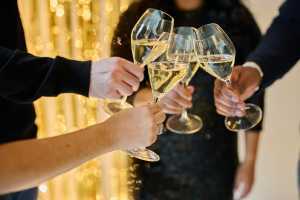 Sparkling wine | Hands clink glasses of sparkling wine in front of a gold background