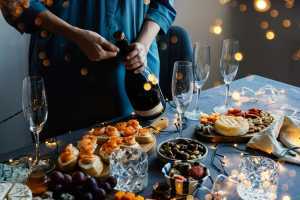 Sparkling wine | A hand opens a bottle of sparkling wine on a spread of food and festive nibbles Sparkling wine | A hand opens a bottle of sparkling wine on a spread of food and festive nibbles