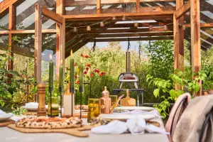 The Ooni Karu 12G pizza oven in a garden behind a set table with pizzas The Ooni Karu 12G pizza oven in a garden behind a set table with pizzas