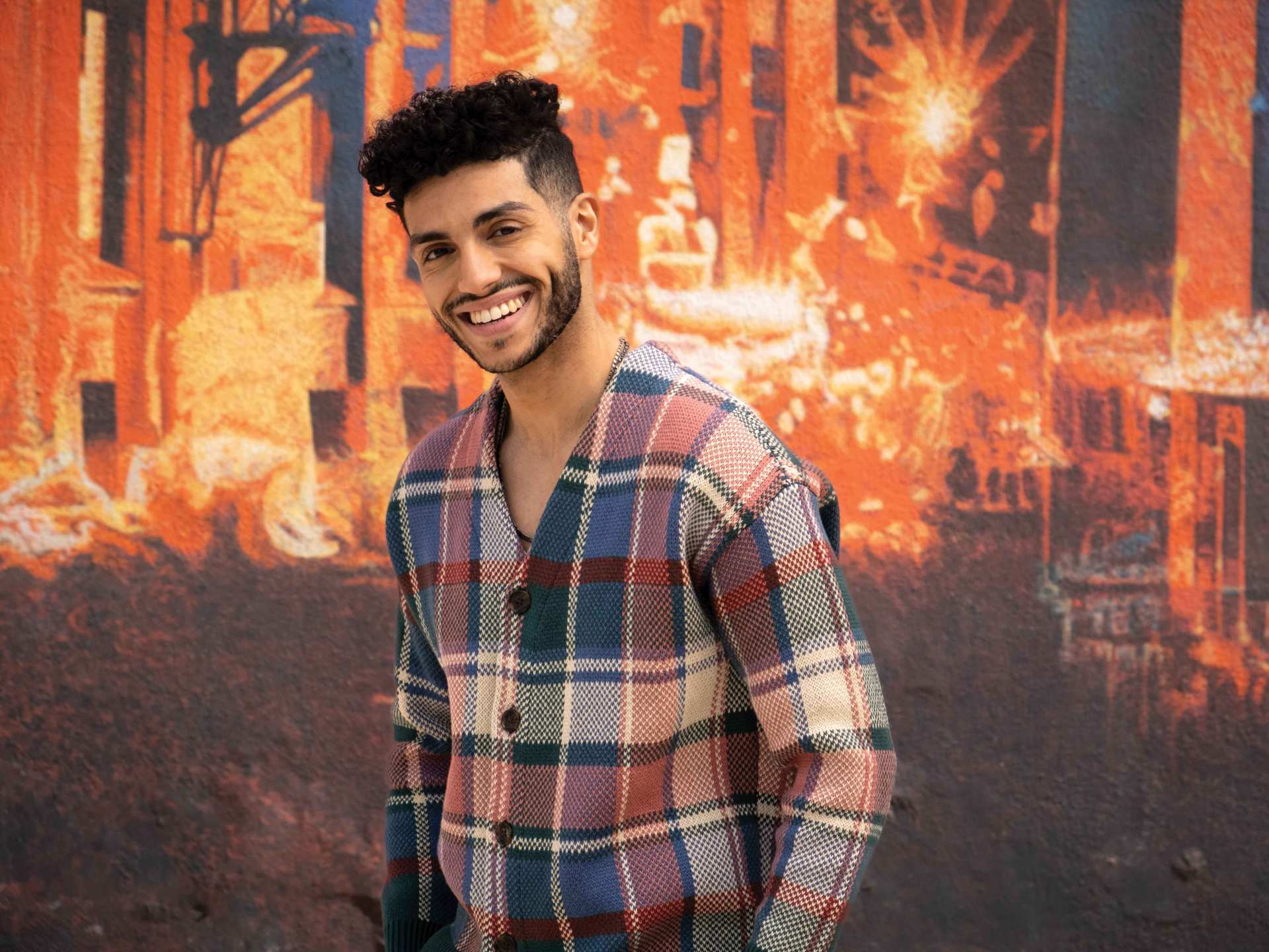 Vegan food in Toronto | Mena Massoud smiling in front of a colourful wall Vegan food in Toronto | Mena Massoud smiling in front of a colourful wall