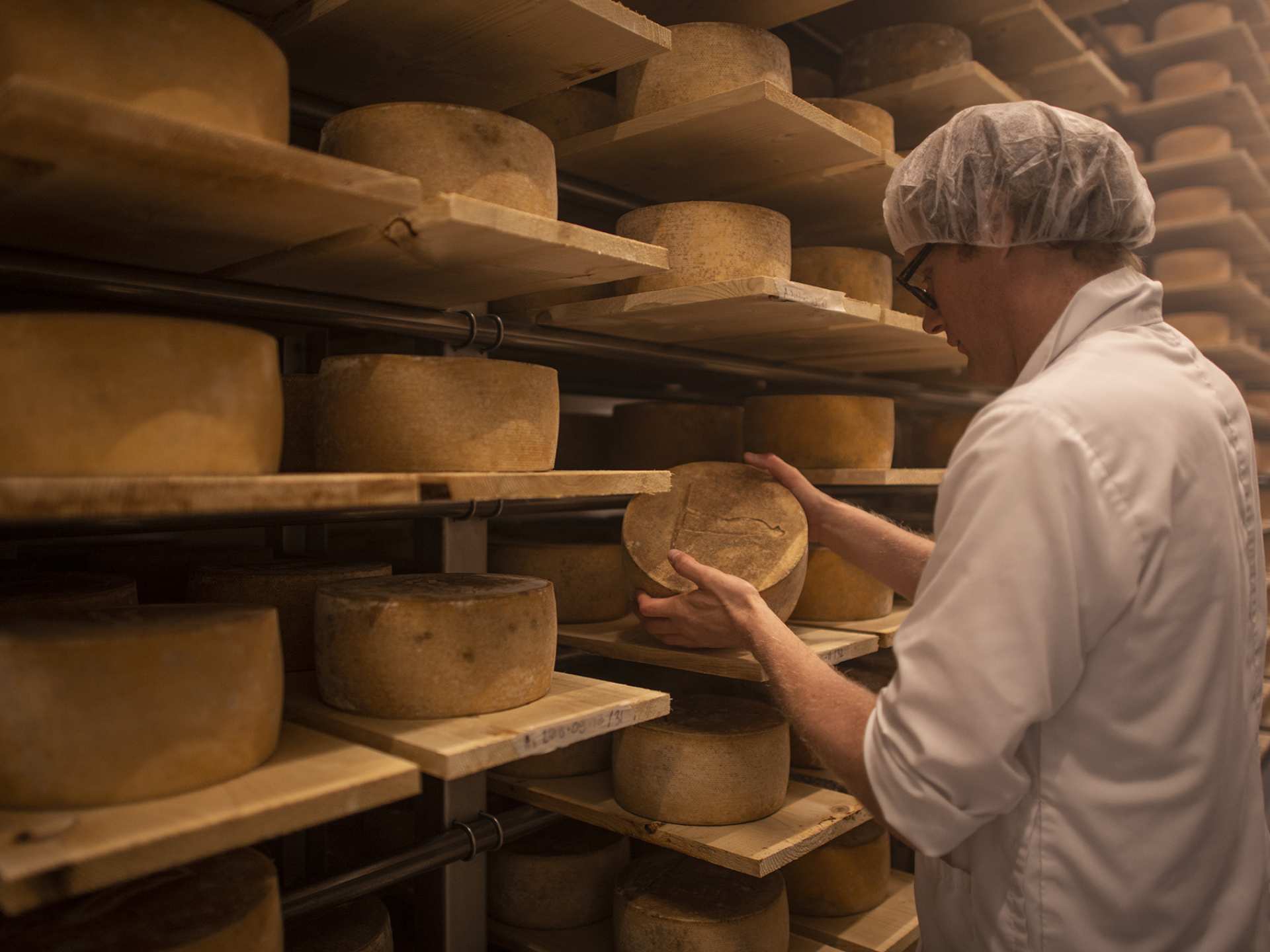 A Québecois cheesemaker examining a wheel of cheese A Québecois cheesemaker examining a wheel of cheese