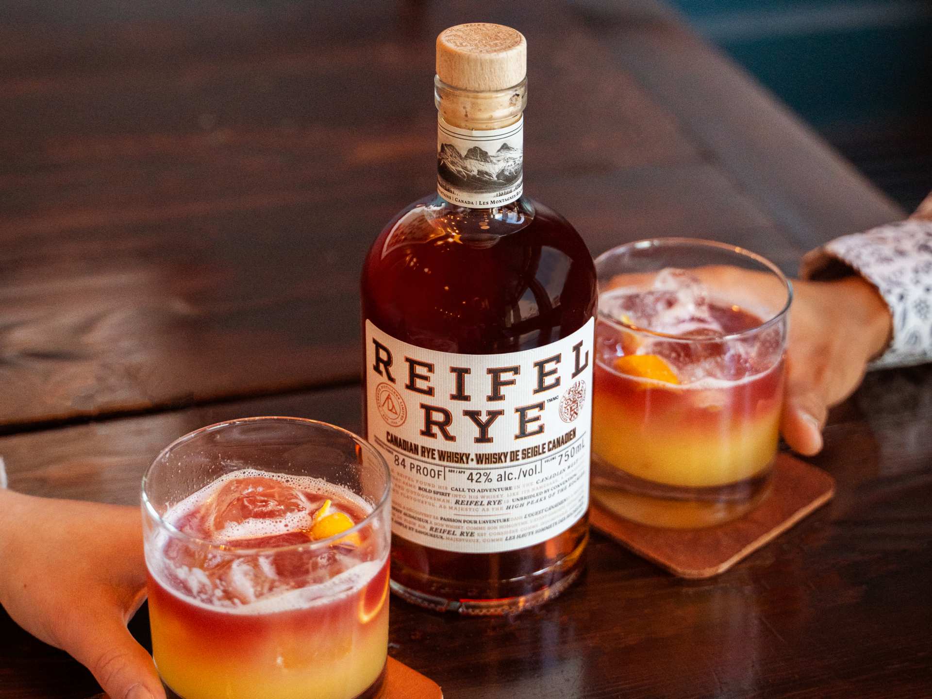 A bottle of Reifel Rye with two sour cocktails
