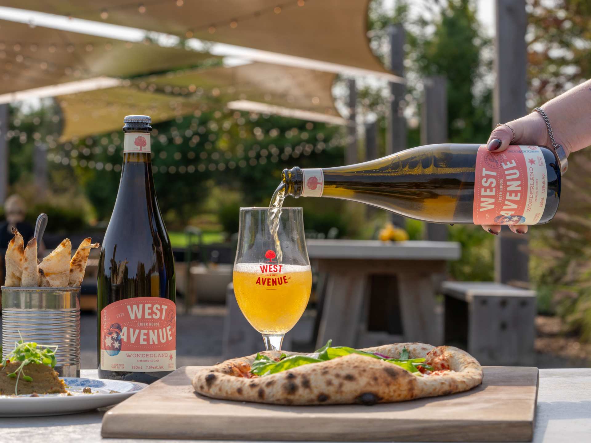 Support local with Feast On | A West Avenue Cider is poured in front of a pizza on a patio Support local with Feast On | A West Avenue Cider is poured in front of a pizza on a patio