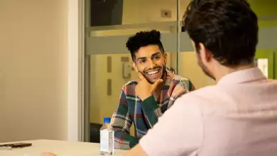 Mena Massoud | Aladdin actor Mena Massoud smiling and sitting at a table