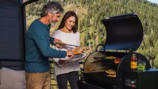 A couple cooks salmon on a Traeger grill