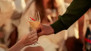 A glass of G. H. Mumm champagne is extended from one hand to another A glass of G. H. Mumm champagne is extended from one hand to another