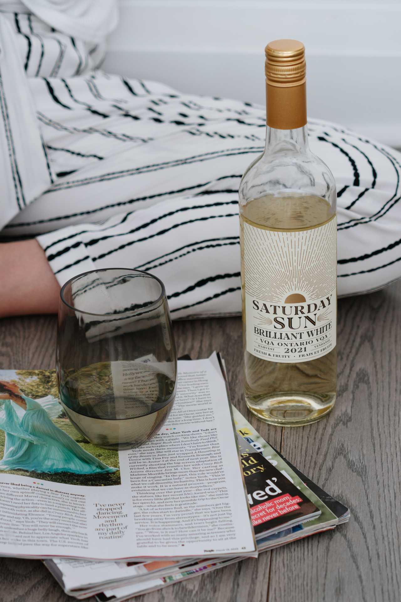 A bottle of Saturday Sun Brilliant White Harvest VQA with a glass and a book