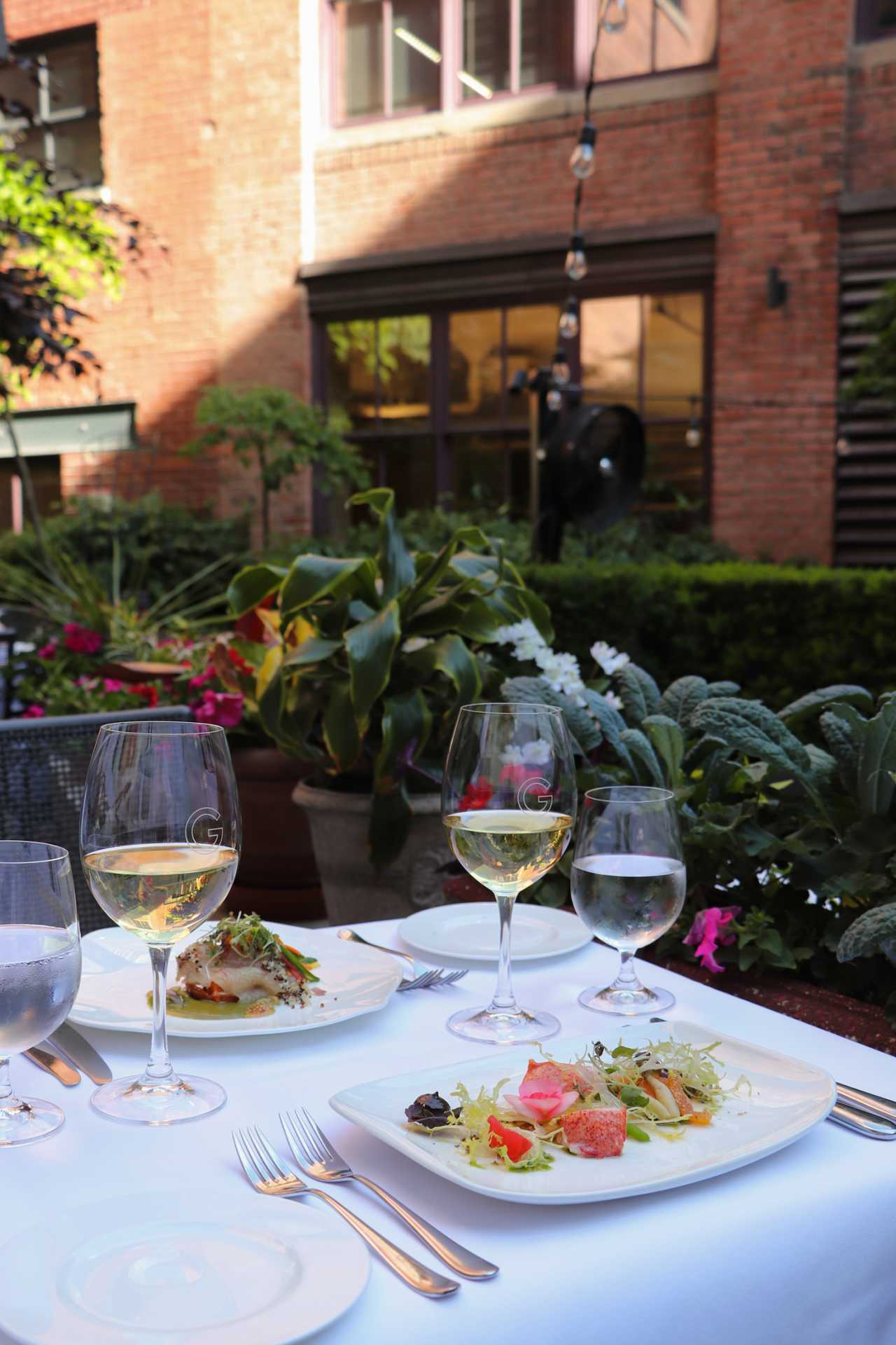 George Restaurant | Glasses of wine sit on a table alongside a plates from a patio exclusive menu in George Restaurant's courtyard patio