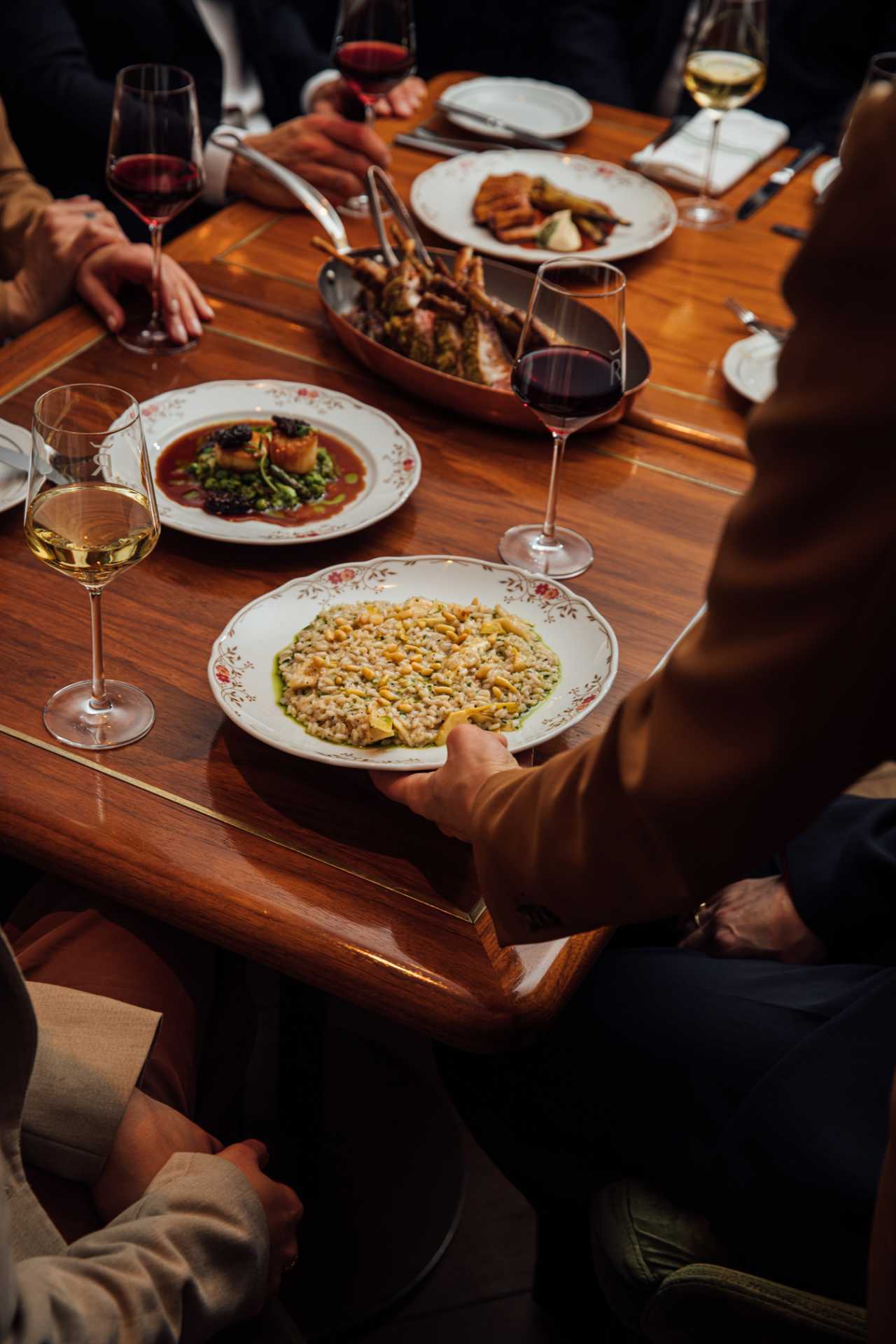 REIGN Toronto | A hand delivers a plate of risotta to a table spread with food and wine at REIGN