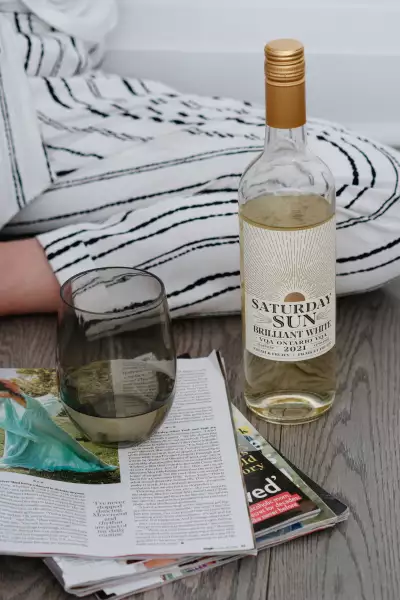 A bottle of Saturday Sun Brilliant White Harvest VQA with a glass and a book