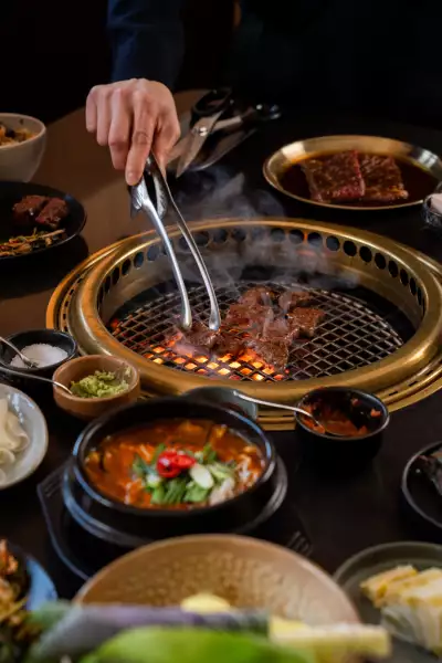 Takja BBQ | A hand using tongs to turn meat at Takja BBQ