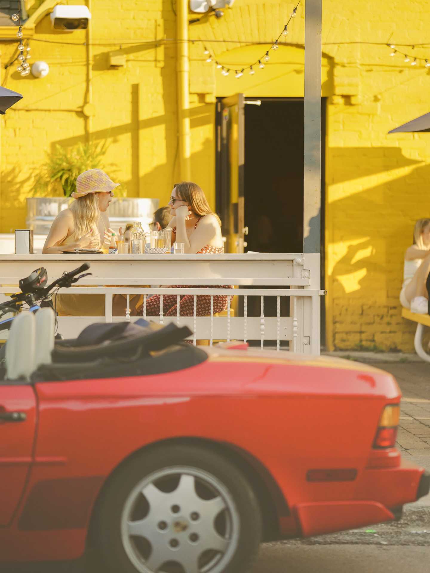 The best bars in Toronto | A car parked outside of Pennies, guests enjoying the patio