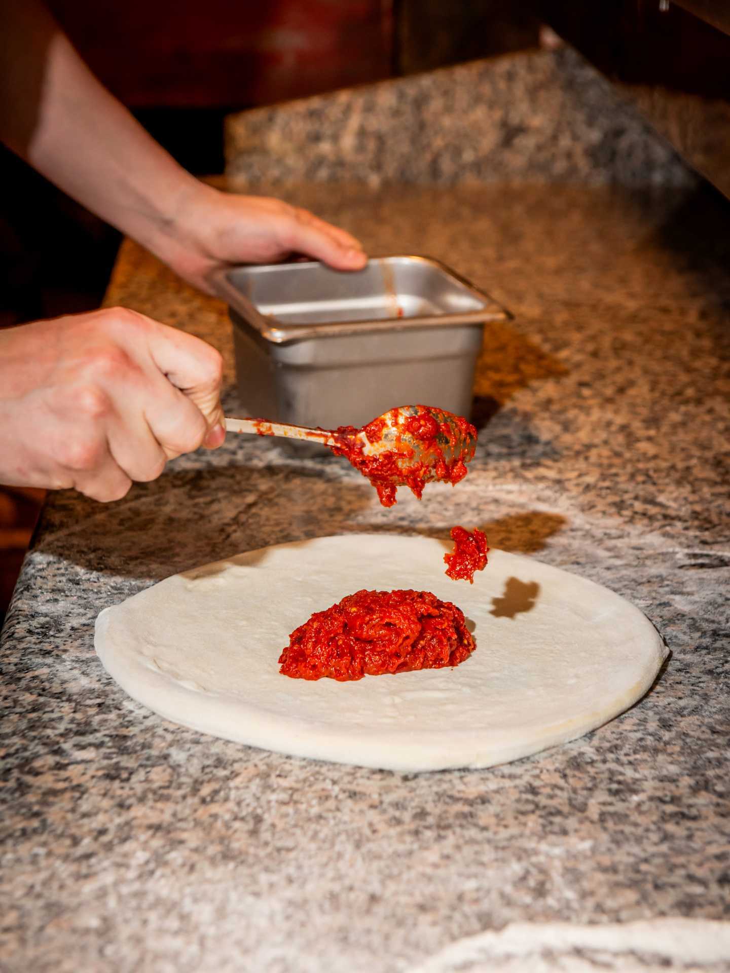 Toronto pizza | Spreading the sauce onto a pizza at Pizza e Pazzi