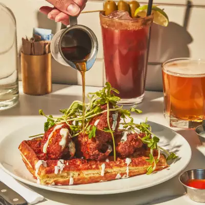 Maple syrup being poured on a stack of chicken and waffles at The Drake