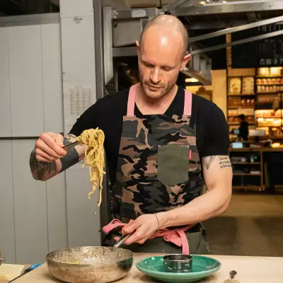 Ruben Rapetti holding a forkful of spaghetti wearing a camo apron