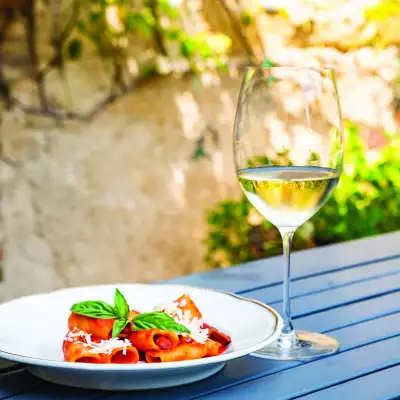 A beautiful plate of pasta on a table with a glass of white Sicilia DOC wine