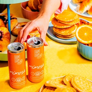 Two cans of Sunday Funday Mimosa with a brunch spread Two cans of Sunday Funday Mimosa with a brunch spread