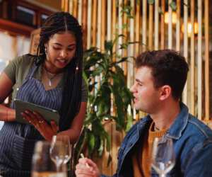 The Re-Seasoning Coalition | A customer listens to a waitress holding a tablet at a restaurant