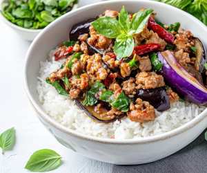 Thai Hom Mali rice | Thai basil eggplant with minced pork served over steamed jasmine rice, garnished with fresh basil leaves and dried red chilies in a white bowl