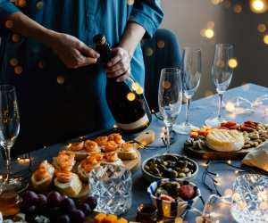 Sparkling wine | A hand opens a bottle of sparkling wine on a spread of food and festive nibbles