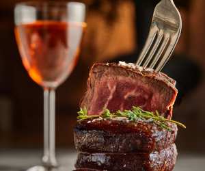 Jacobs & Co. Steakhouse | A fork digs into a piece of steak while a classic cocktail looks on in the background