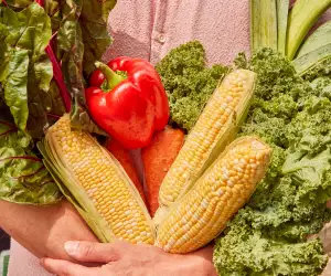 Vegan food Toronto | A person holding carrot, swiss chard and corn with their arms crossed