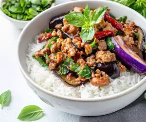 Thai Hom Mali rice | Thai basil eggplant with minced pork served over steamed jasmine rice, garnished with fresh basil leaves and dried red chilies in a white bowl