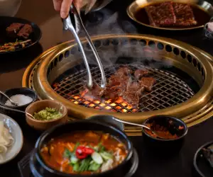 Takja BBQ House | An hand uses tongs to flip a piece of prime meat at Takja BBQ House